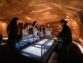 Students crowd around an exhibit on a visit to The National Library of New Zealand, Te puna Mātauranga o Aotearoa. Anna Tiaki facilitating tour of He Tohu.