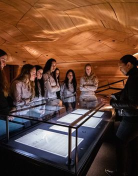 Students crowd around an exhibit on a visit to The National Library of New Zealand, Te puna Mātauranga o Aotearoa. Anna Tiaki facilitating tour of He Tohu.