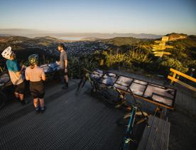 3 bikers standing on the summit of Mākara Peak Mountain Bike Park, looking over the Wellington Harbour.