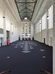 A conference hall at Massey University in Mount Cook, Wellington. The large space is empty with a blue carpet and white walls. There are three rows of hanging lights from the high ceiling.