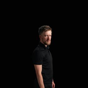 Daniel Sloss looks toward the camera with a black background.