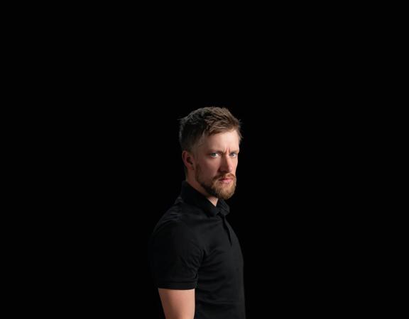 Daniel Sloss looks toward the camera with a black background.