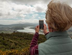 A person uses their smartphone to take a picture of the scenic view from the peak of Rangituhi / Colonial Knob Walkway.