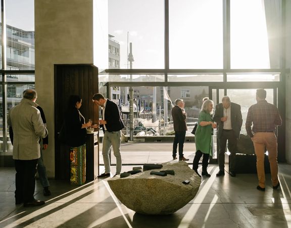People mingle inside the James Blackie Gallery as sunlight spills into the space from outside.