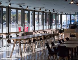 A bar set up inside Lower Hutt Events Centre, with wooden high tables and normal tables, and large glass windows.