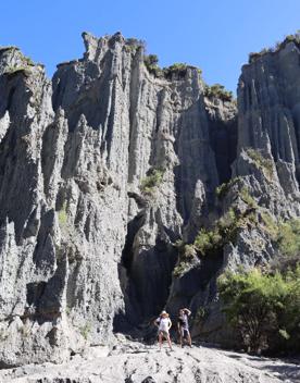 Two people stand at the base of a large rock face at the Putangirua Pinnacles track in the Wairarapa. 