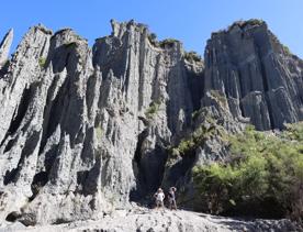 Two people stand at the base of a large rock face at the Putangirua Pinnacles track in the Wairarapa.