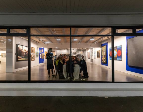 Looking into the front window of Webb's Wellington Conference Venue where a group of people sit at a long table and contemporary art paintings are on the walls.