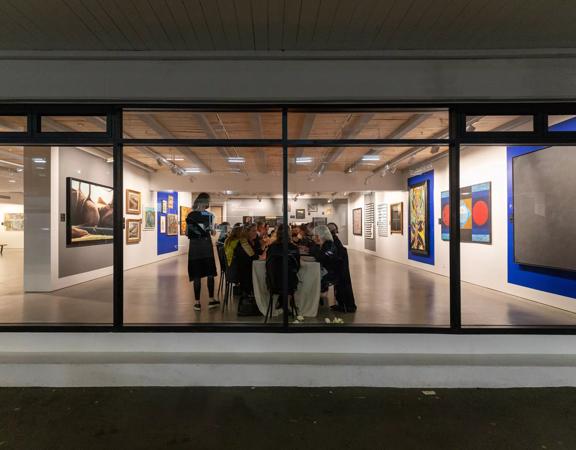 Looking into the front window of Webb's Wellington Conference Venue where a group of people sit at a long table and contemporary art paintings are on the walls. 