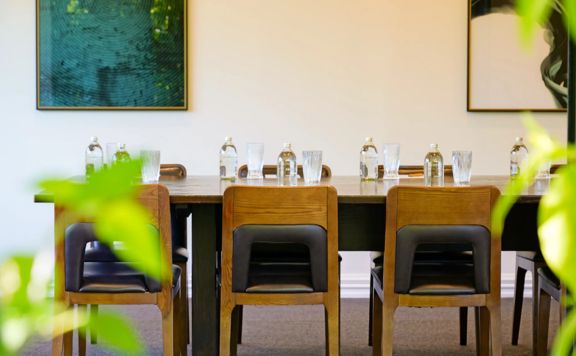 A dining table is set with glasses and bottles of water. Two pieces of art hang on the wall behind.