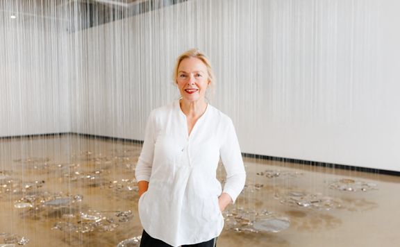 Andrea Schlieker in a white room with an art installation suspended in the background.