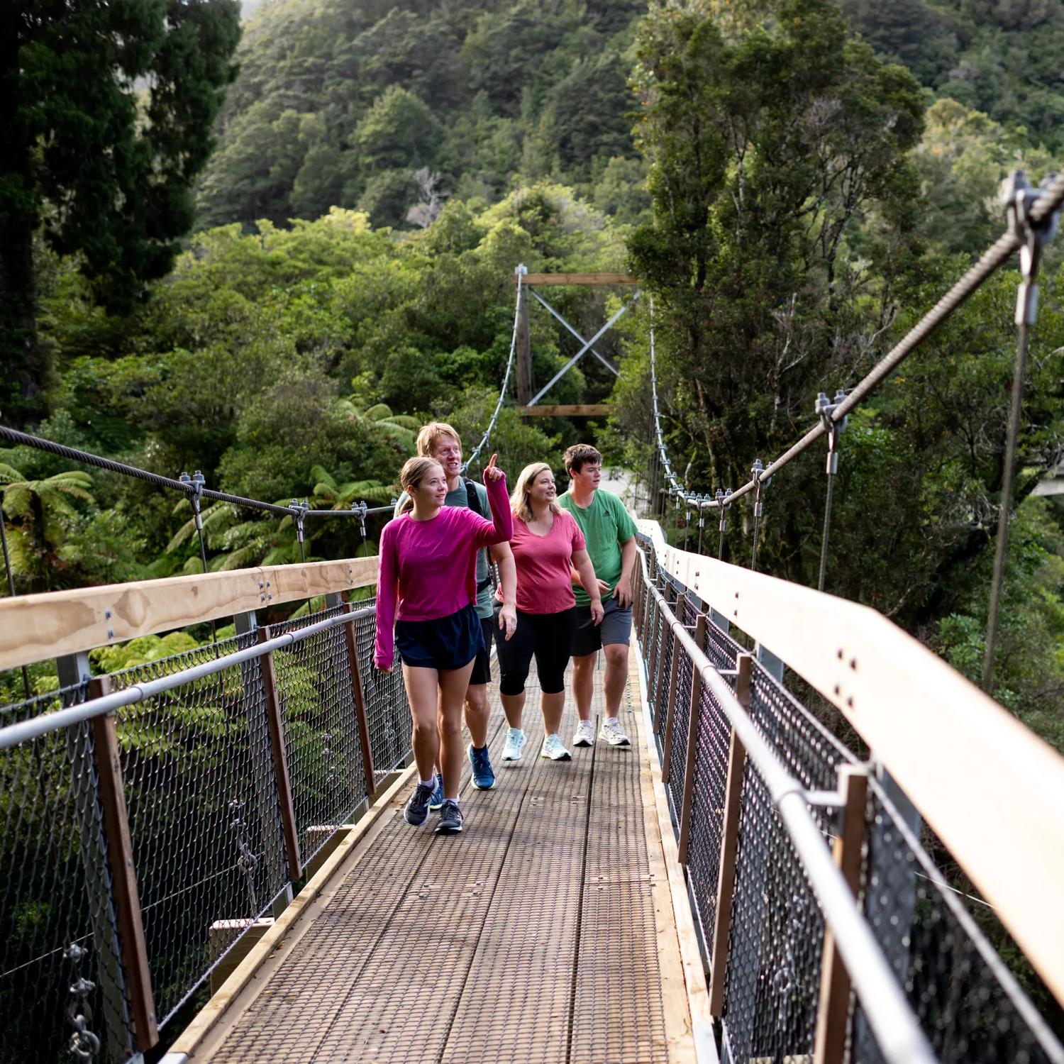 People walking along one of the two swing bridges over the river amongst trees in Kaitoke Regional Park.