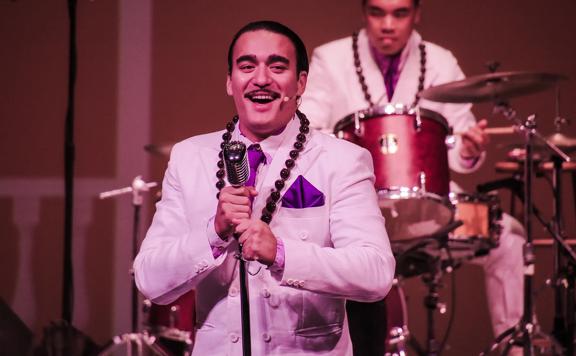 A Hawaiian singer in a purple suit performing on stage.
