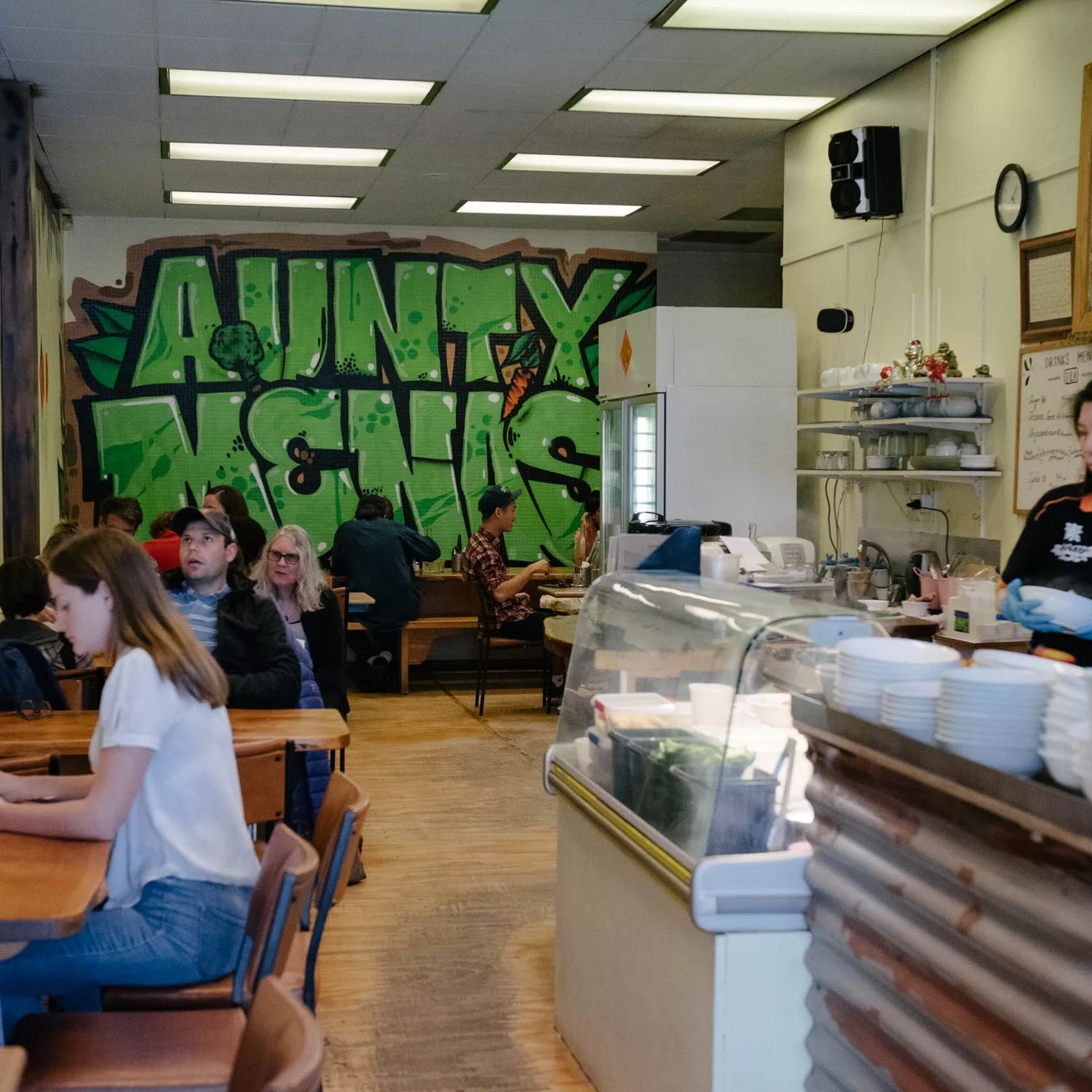 Inside Aunty Mena's, a small vegetarian Malaysian restaurant on Cuba Street in Te Aro, Wellington. The restaurant's name is graffitied in big green letters on the back wall.