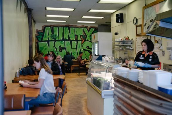 Inside Aunty Mena's, a small vegetarian Malaysian restaurant on Cuba Street in Te Aro, Wellington. The restaurant's name is graffitied in big green letters on the back wall.