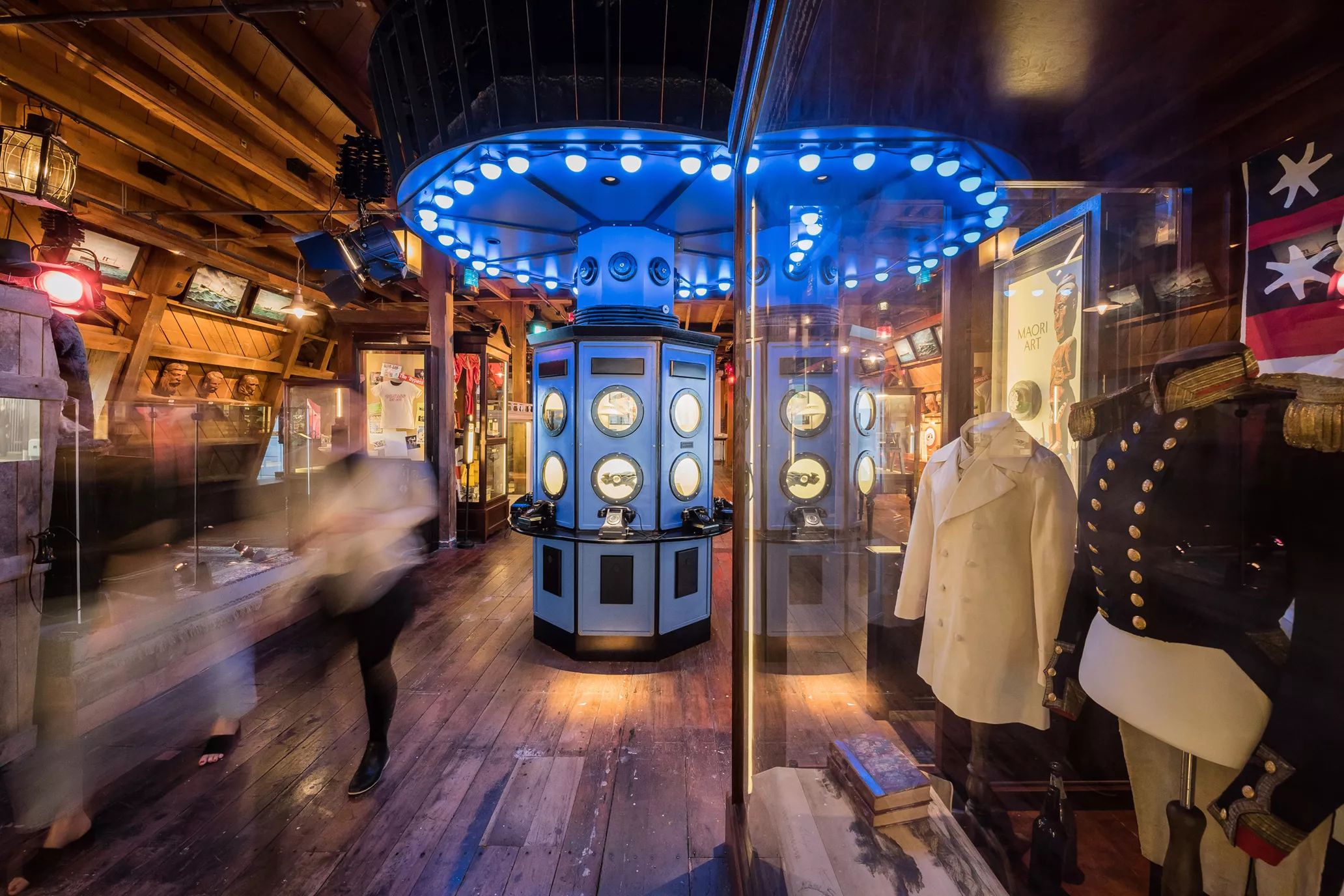 Inside a room at the Wellington Museum with wood flooring, wood-paneled walls and ceiling, two mannequin busts dressed in nautical jackets and three rotary phones displayed on a blue octagonal pillar in the middle of the room.
