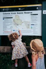 Two kids looking at an informational trail sign. One is climbing on a fence to point on the map.