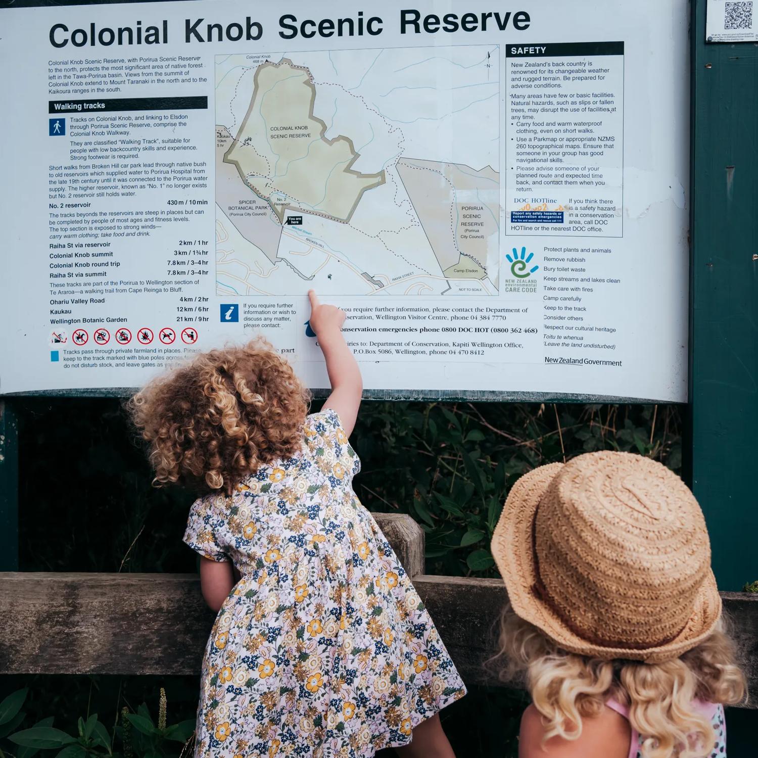 Two kids looking at an informational trail sign. One is climbing on a fence to point on the map.