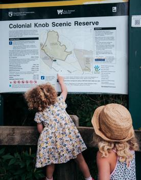 Two kids looking at an informational trail sign. One is climbing on a fence to point on the map.