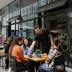 A server delivers coffee and food to a table of three outside Picke & Pie.