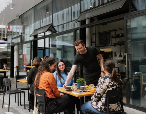 A server delivers coffee and food to a table of three outside Picke & Pie.