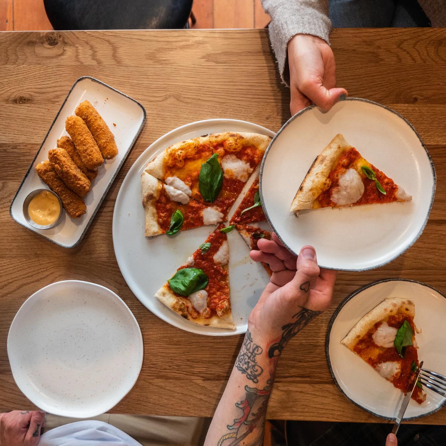 A Margherita pizza being shared and mozzarella sticks.