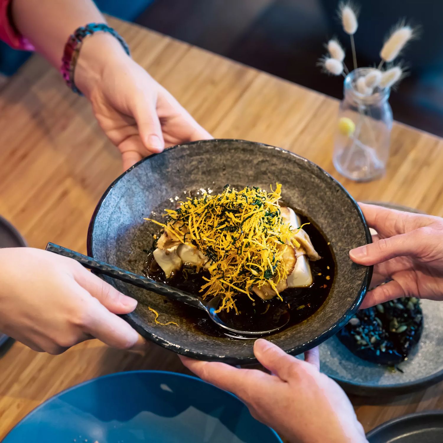 A dish of dumplings being passed from one pair of hands to another over a table at Koji, an Asian-fusion restaurant in Mount Victoria, Wellington, New Zealand.
