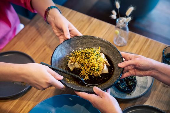 A dish of dumplings being passed from one pair of hands to another over a table at Koji, an Asian-fusion restaurant in Mount Victoria, Wellington, New Zealand.