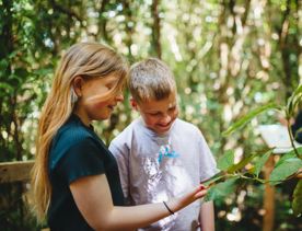 Two kids inspect a leafy branch while exploring Zealandia.