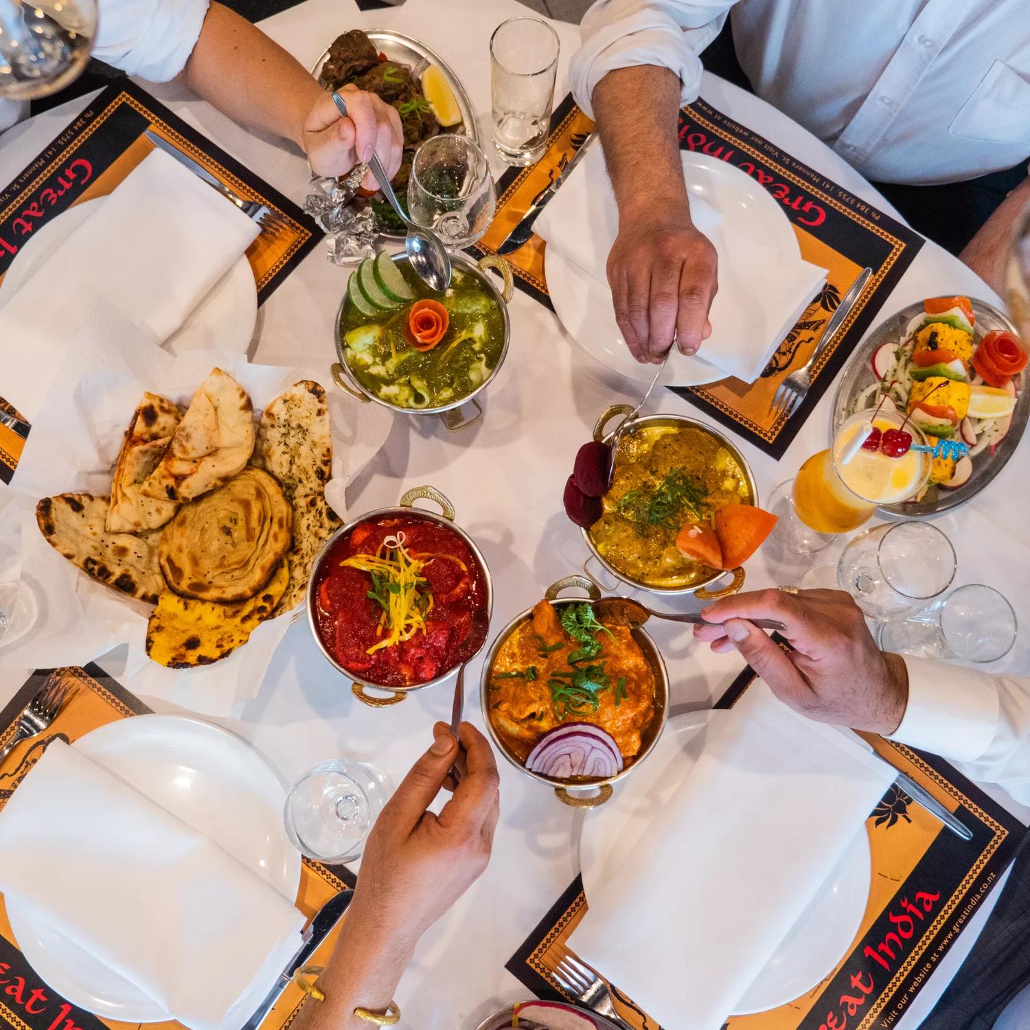 4 hands serve their meals onto their plates at Great India Restaurant.