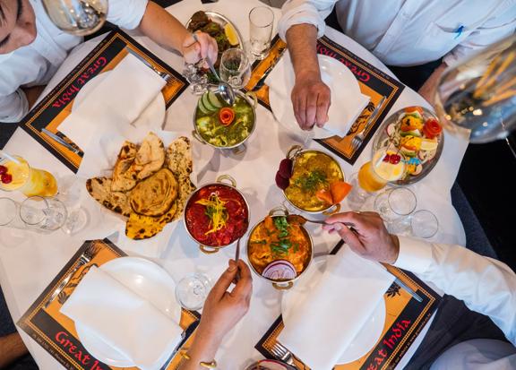 4 hands serve their meals onto their plates at Great India Restaurant.