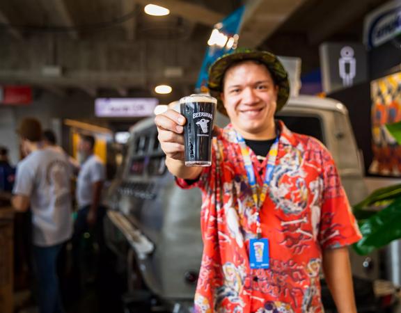 Person holding a Beervana beer out in front of him, smiling at the camera.
