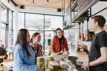 Three smiling customers order at the counter of Pickle & Pie.
