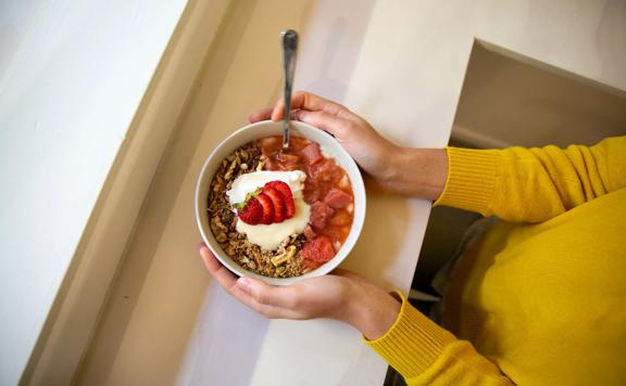 Hands holding a bowl made by The Oatery, topped with strawberries and granola.