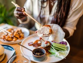 A person uses chopsticks to place a piece of Peking duck into a wrap during a meal at Hei.