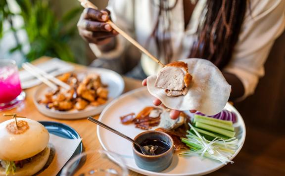 A person uses chopsticks to place a piece of Peking duck into a wrap during a meal at Hei.