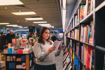 A person reads a book inside Unity books, while standing in front of a colourful bookshelf.