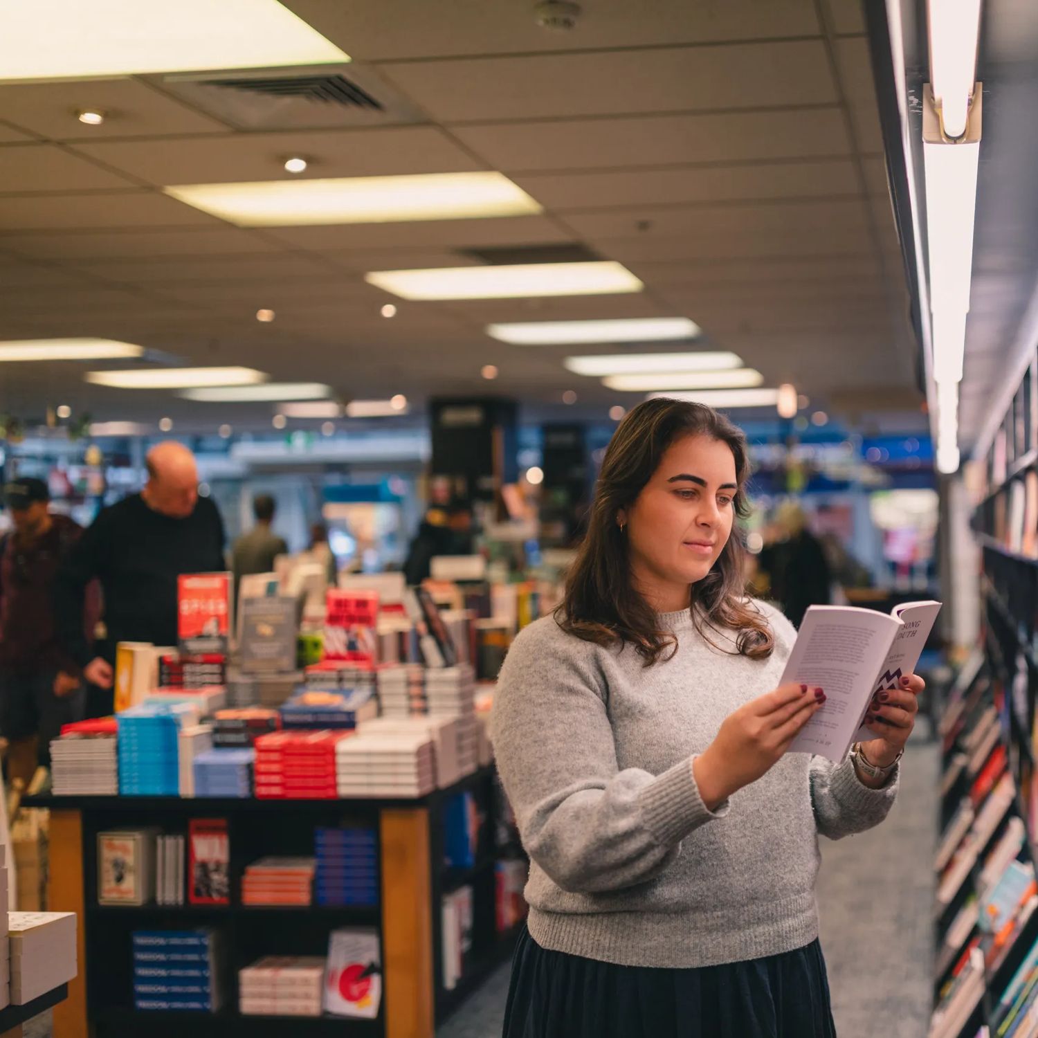 A person reads a book inside Unity books, while standing in front of a colourful bookshelf.