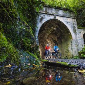 Two bikers going through a dark tunnel on the Rail Trail Section on the Remutaka Cycle Trail.
