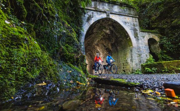 Two bikers going through a dark tunnel on the Rail Trail Section on the Remutaka Cycle Trail.