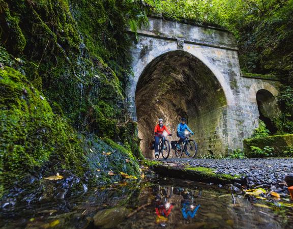 Two bikers going through a dark tunnel on the Rail Trail Section on the Remutaka Cycle Trail.