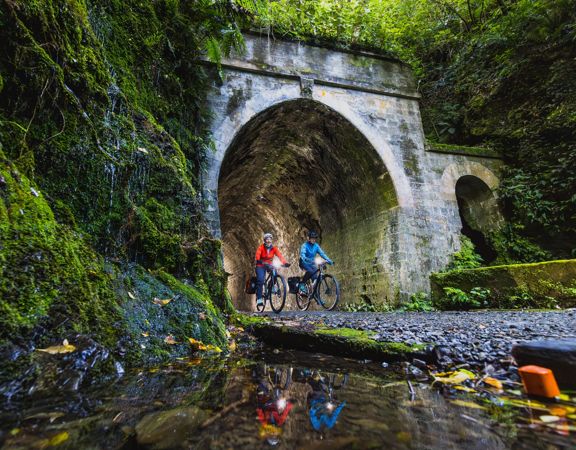 Two bikers going through a dark tunnel on the Rail Trail Section on the Remutaka Cycle Trail.