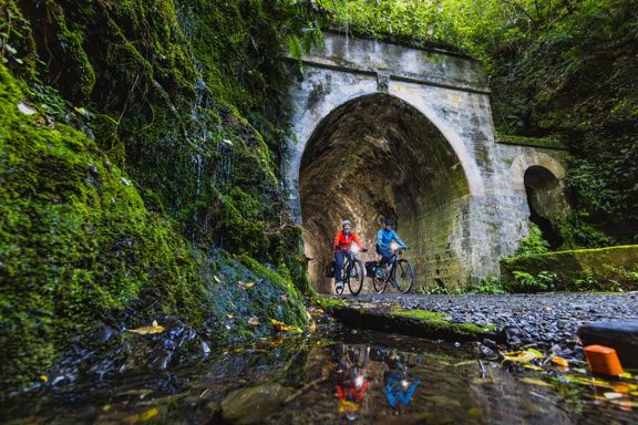 Two bikers going through a dark tunnel on the Rail Trail Section on the Remutaka Cycle Trail.