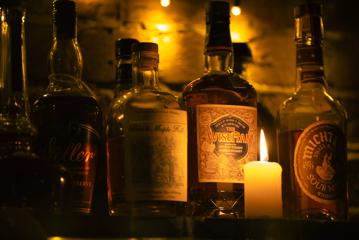 Four bottles of assorted whiskeys and a small burning candle on a shelf.