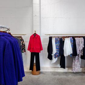 The interior of Twenty-Seven Names, a clothing store located on Ghuznee Street and Marion Street in Wellington, with three clothing racks full of blue, black, fuchsia, white and floral pattern women's blouses and dresses and one outfit displayed independe