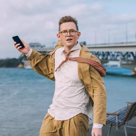 Chris Parker posing with a phone in front of a bridge.