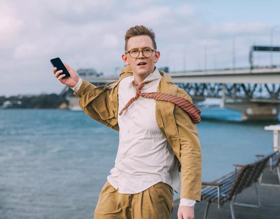 Chris Parker posing with a phone in front of a bridge.