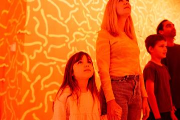 A family walks inside an orange room at the Dowse Museum.