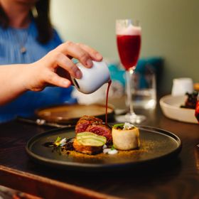 Person pouring red wine jus over a fancy plate of food