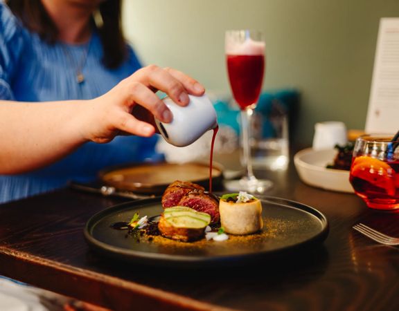 Person pouring red wine jus over a fancy plate of food